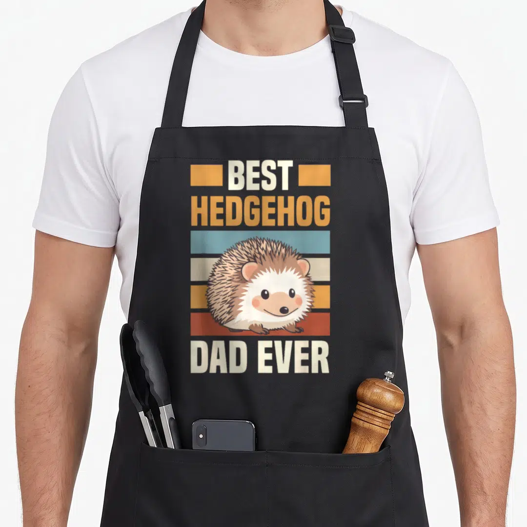 Prickly animal apron - Cartoon hedgehog over orange blue red stripes with best hedgehog dad ever text — shown on a black cotton canvas apron against a white background