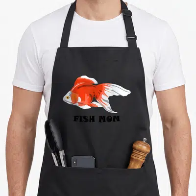Fish silly apron - Orange and white cartoon goldfish above black FISH MOM text — shown on a black cotton canvas apron against a white background