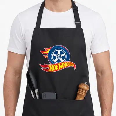 Flaming wheel apron - Blue car wheel with red and yellow flames and Hot Wheels logo below — shown on a black cotton canvas apron against a white background