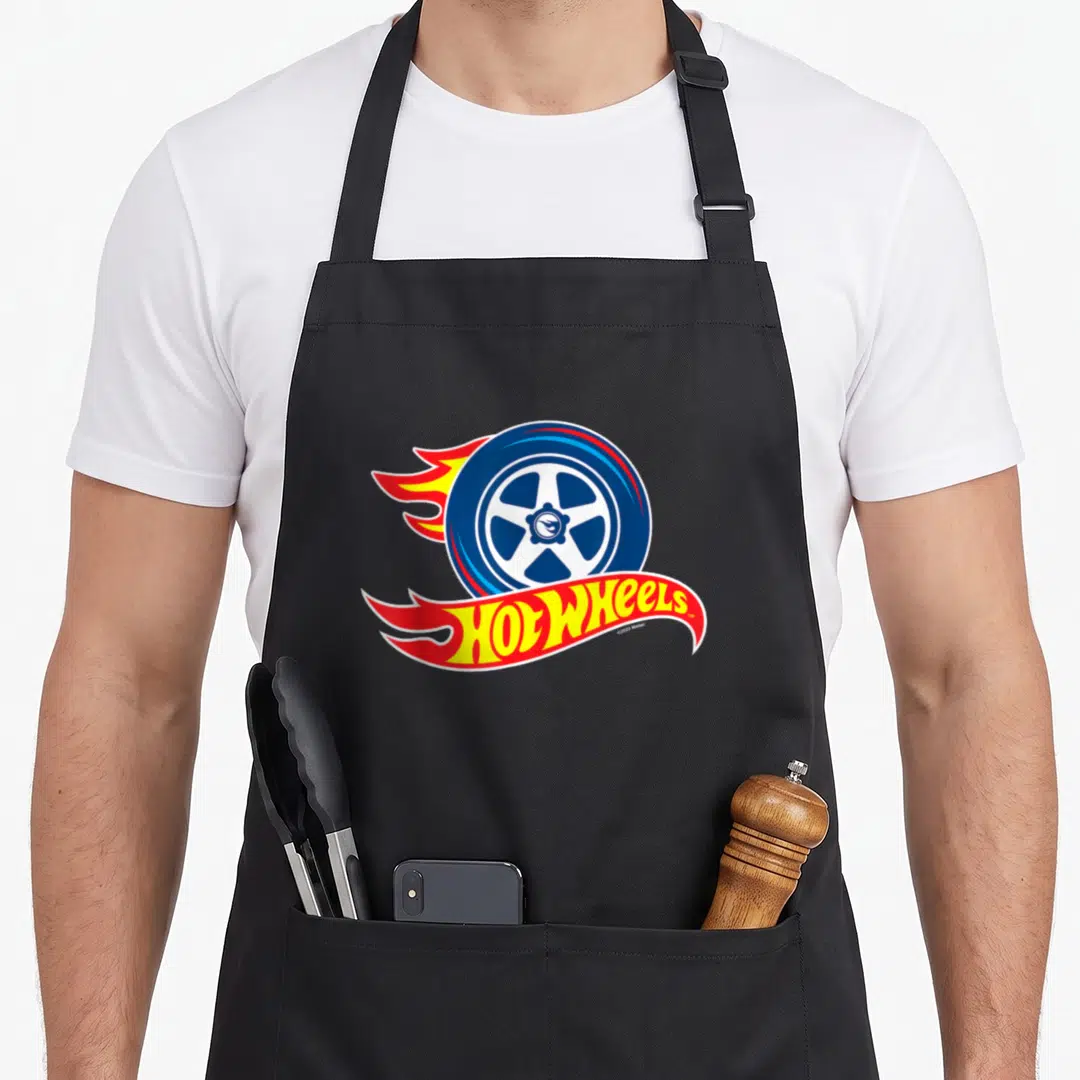 Flaming wheel apron - Blue car wheel with red and yellow flames and Hot Wheels logo below — shown on a black cotton canvas apron against a white background