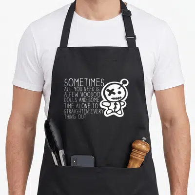 Sometime doll apron - White cartoon voodoo doll with X eye next to stacked text about straightening things out — shown on a black cotton canvas apron against a white background