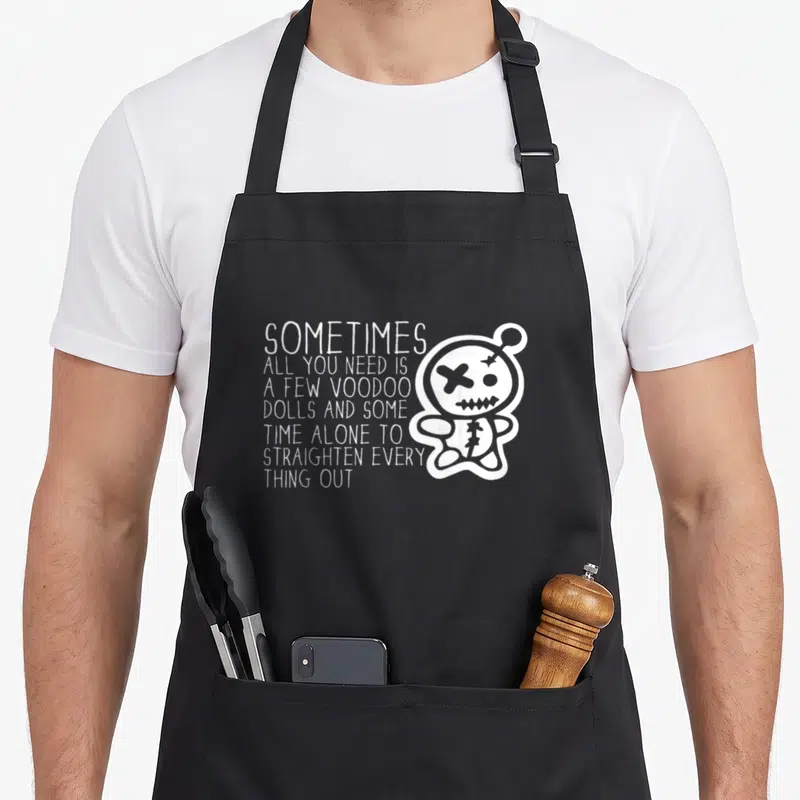 Sometime doll apron - White cartoon voodoo doll with X eye next to stacked text about straightening things out — shown on a black cotton canvas apron against a white background