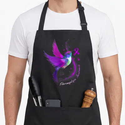 Hummingbird fibromyalgia ribbon apron - Realistic hummingbird holding purple ribbon with Fibromyalgia Awareness text — shown on a black cotton canvas apron against a white background