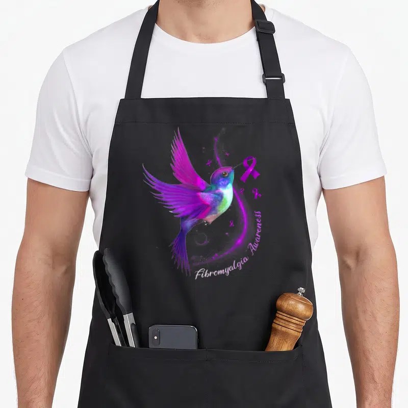Hummingbird fibromyalgia ribbon apron - Realistic hummingbird holding purple ribbon with Fibromyalgia Awareness text — shown on a black cotton canvas apron against a white background