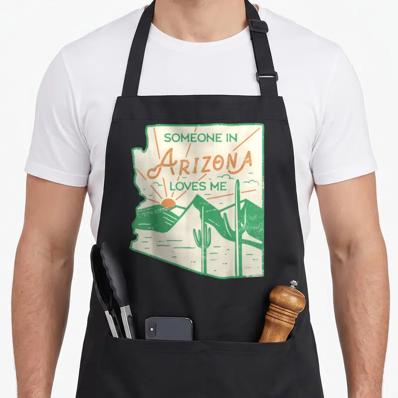 Someone arizona apron - Retro Arizona state outline with cacti, mountains, and rising sun in green and orange — shown on a black cotton canvas apron against a white background
