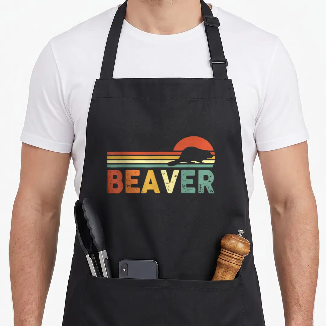 80s beaver apron - Grey beaver silhouette over orange sun and stripes with multi-colored BEAVER text — shown on a black cotton canvas apron against a white background