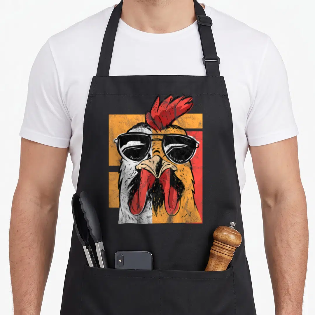 Sunglass rooster apron - Retro rooster head with sunglasses on orange and red geometric background — shown on a black cotton canvas apron against a white background
