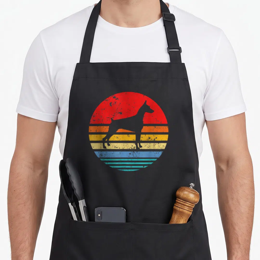 Doberman sunset dog apron - Retro dog silhouette against red orange yellow blue and teal striped sun — shown on a black cotton canvas apron against a white background