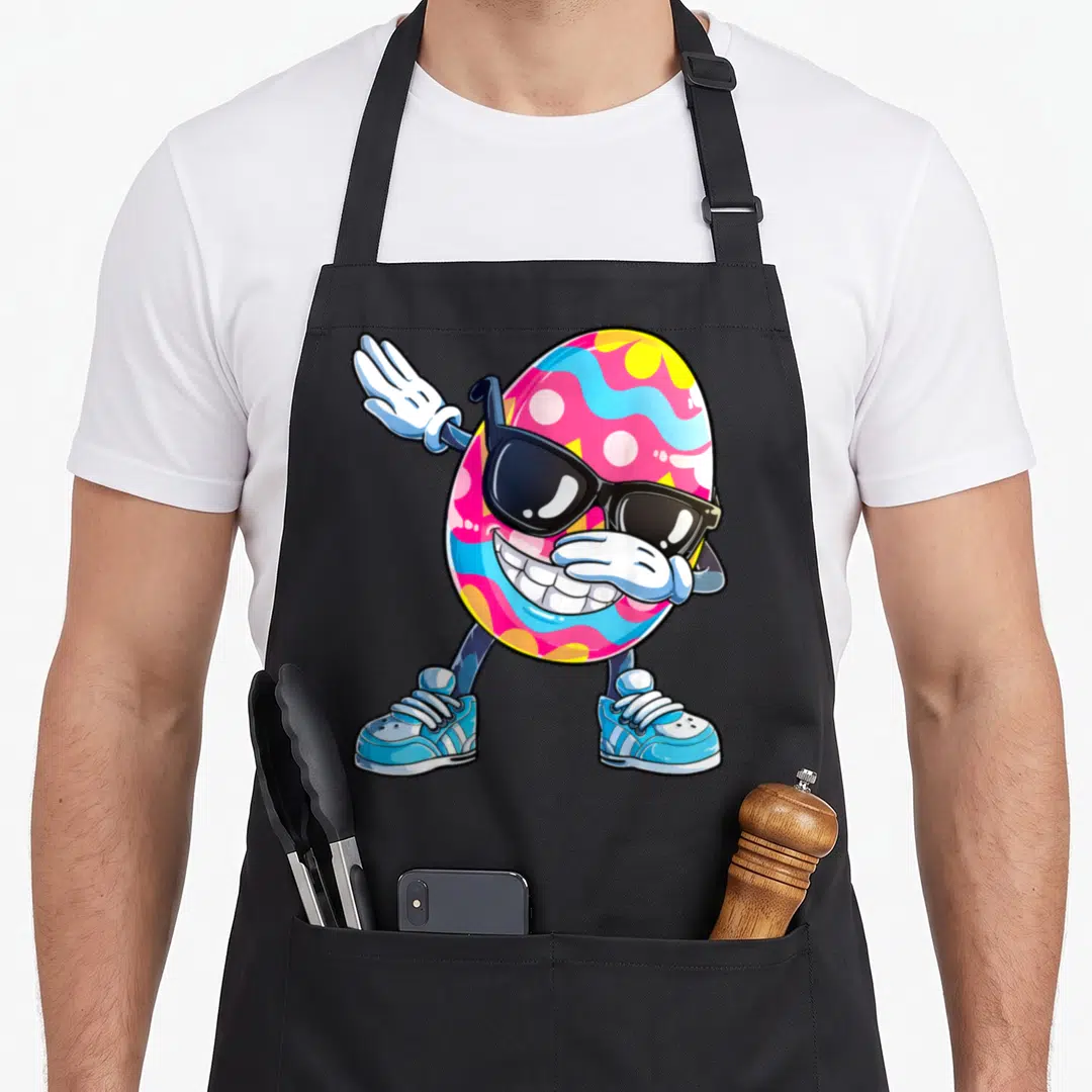 Dabbing egg apron - Cartoon Easter egg wearing sunglasses and sneakers performing the dab dance pose in pink and blue — shown on a black cotton canvas apron against a white background