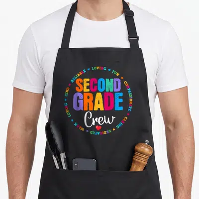 Grade crew 2nd apron - Colorful stacked text SECOND GRADE Crew surrounded by adjectives and hearts — shown on a black cotton canvas apron against a white background