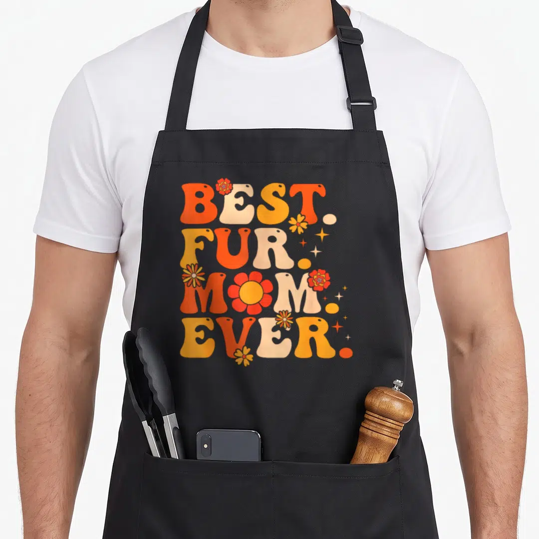Funny fur funny cat aprons - Retro stacked text BEST FUR MOM EVER with orange flowers and yellow stars — shown on a black cotton canvas apron against a white background