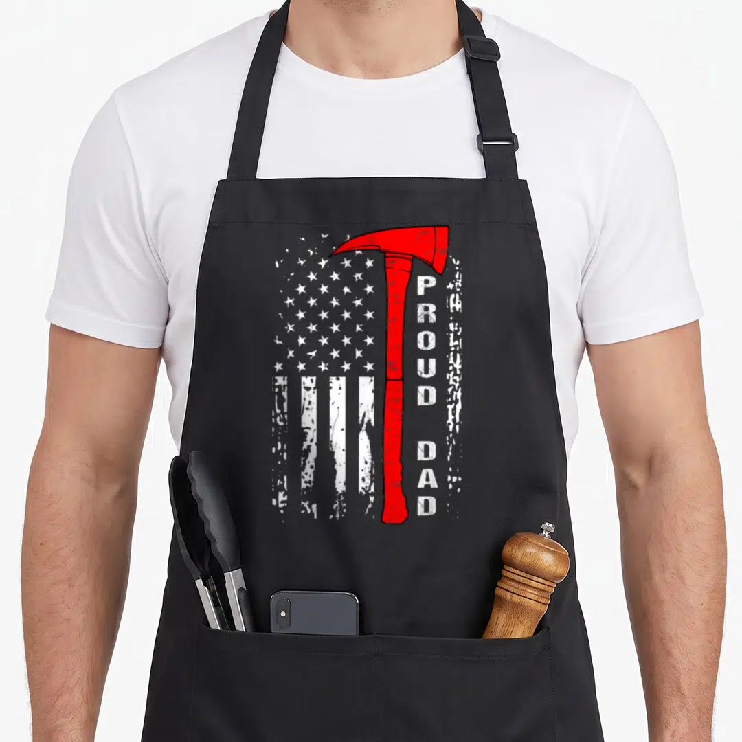 Brave firefighter aprons - Red fire axe with white stars stripes and vertical proud dad text on black — shown on a black cotton canvas apron against a white background