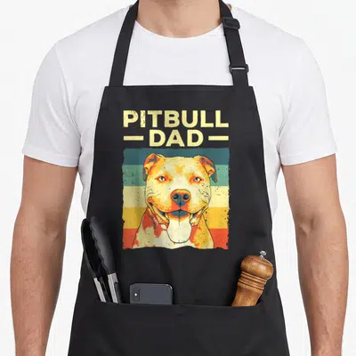 Pitbull father dog apron - Retro pitbull portrait below stacked PITBULL - DAD - text over horizontal yellow, teal — shown on a black cotton canvas apron against a white background