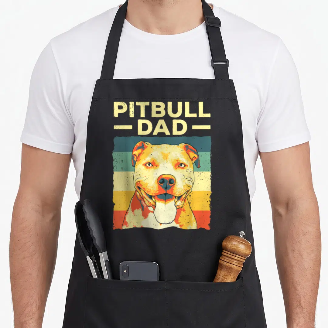 Pitbull father dog apron - Retro pitbull portrait below stacked PITBULL - DAD - text over horizontal yellow, teal — shown on a black cotton canvas apron against a white background