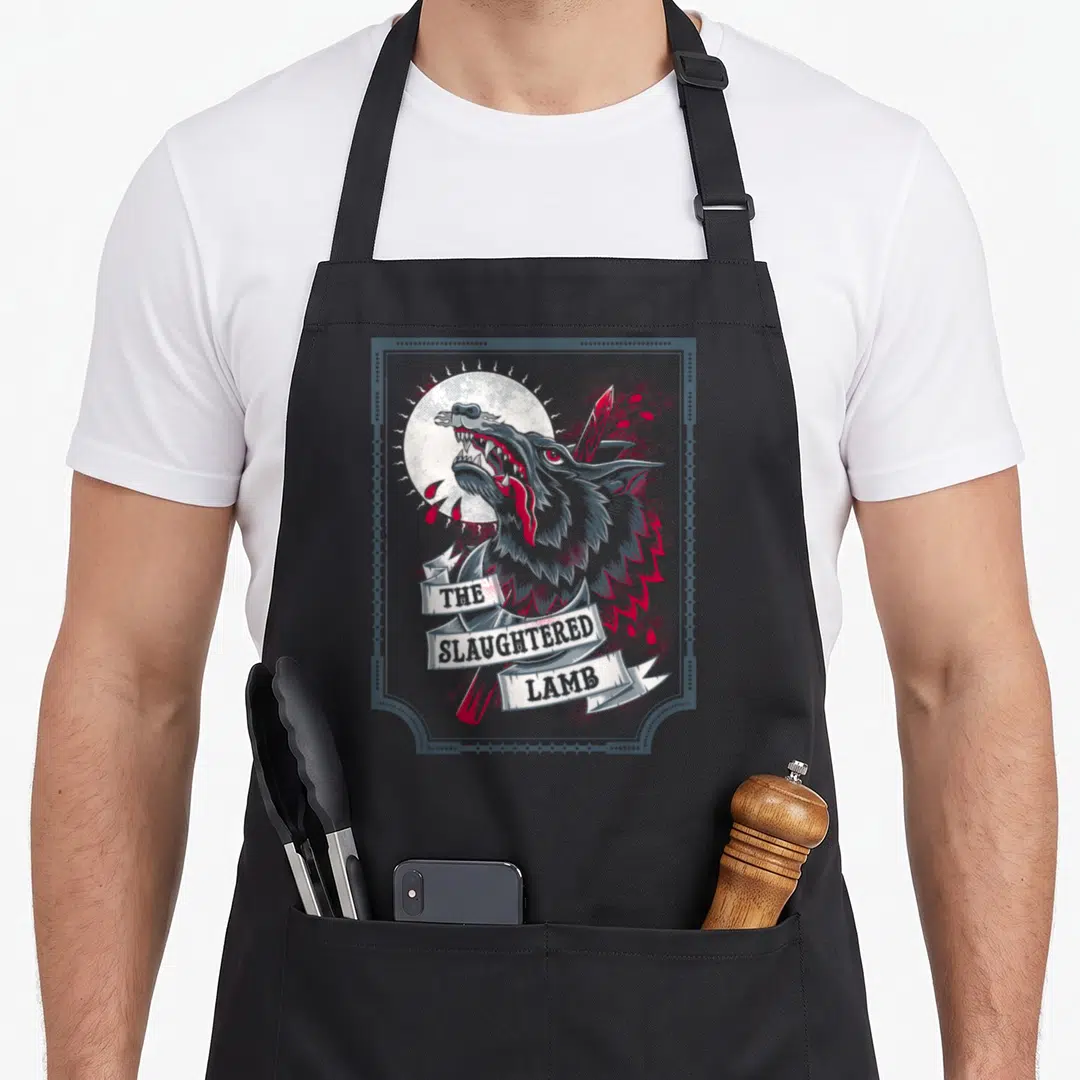 Slaughtered beer apron - Stacked banner text reading THE SLAUGHTERED LAMB over a howling wolf head and knife — shown on a black cotton canvas apron against a white background
