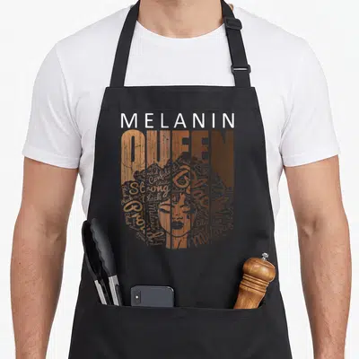Afro african american aprons - Melanin Queen face formed from words Strong Proud Confident in brown tan white black — shown on a black cotton canvas apron against a white background