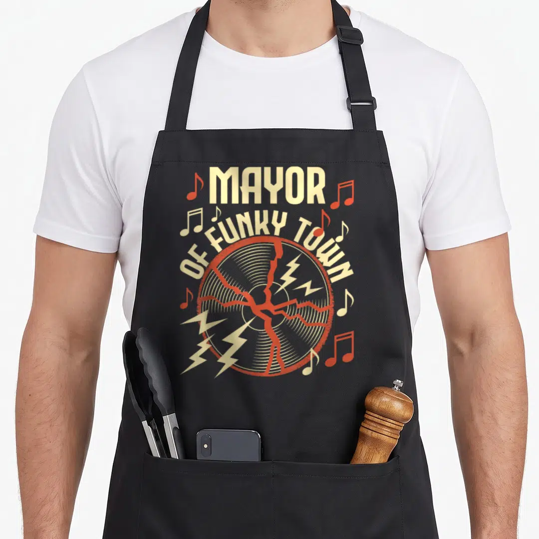 Groove funky apron - MAYOR OF FUNKY TOWN text over cracked vinyl record with red lightning bolts and musical notes — shown on a black cotton canvas apron against a white background