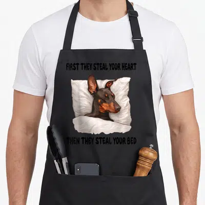 Sleeping doberman apron - Cartoon dog lying on pillow under blanket with text first they steal your heart then they — shown on a black cotton canvas apron against a white background