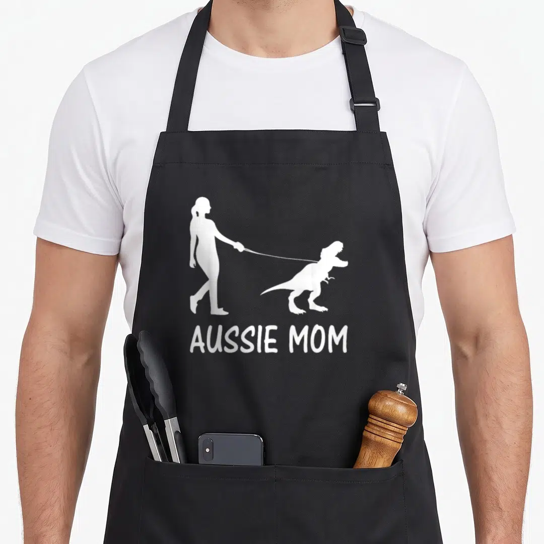 Dinosaur australian aprons - White silhouette of woman walking dinosaur on leash above AUSSIE MOM text — shown on a black cotton canvas apron against a white background