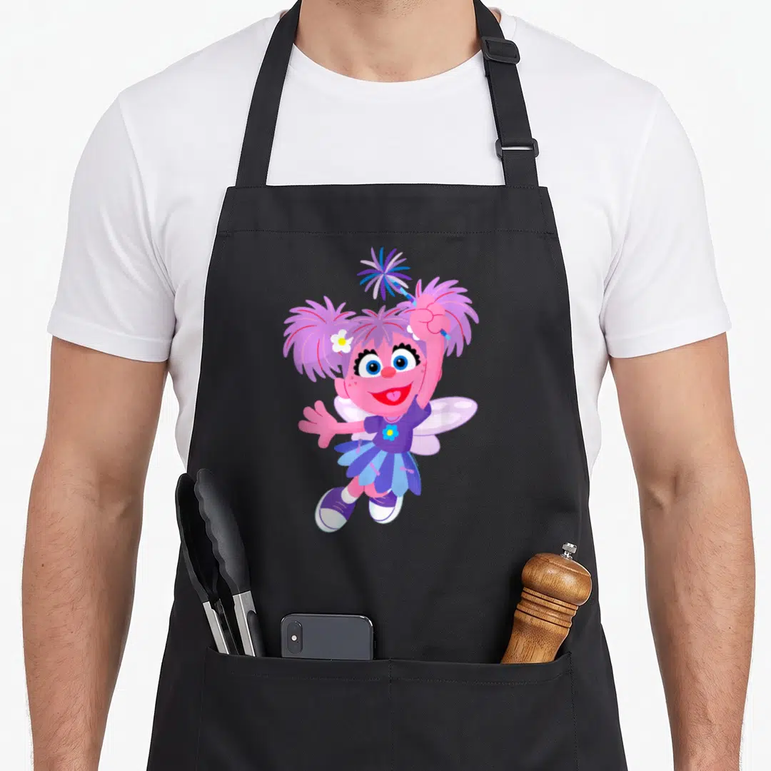 Furry friends apron - Pink fairy character holding a blue and purple pom-pom aloft — shown on a black cotton canvas apron against a white background