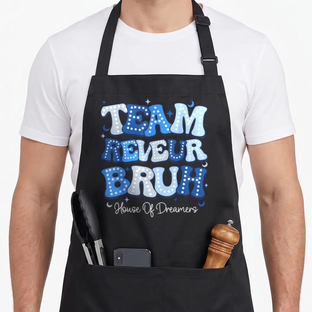 Bruh dreamer apron - Blue bubble text reading TEAM REVEUR BRUH with stars and moons on black fabric — shown on a black cotton canvas apron against a white background