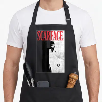 Scarface distressed apron - Red SCARFACE text over a man in a suit against a split black and white background — shown on a black cotton canvas apron against a white background