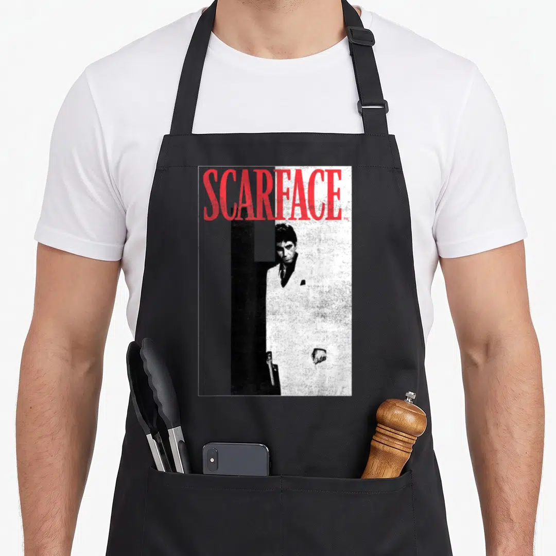 Scarface distressed apron - Red SCARFACE text over a man in a suit against a split black and white background — shown on a black cotton canvas apron against a white background