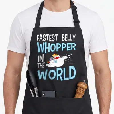 Fastest snowman apron - Rolling snowman with girl rider and stacked text FASTEST BELLY WHOPPER — shown on a black cotton canvas apron against a white background