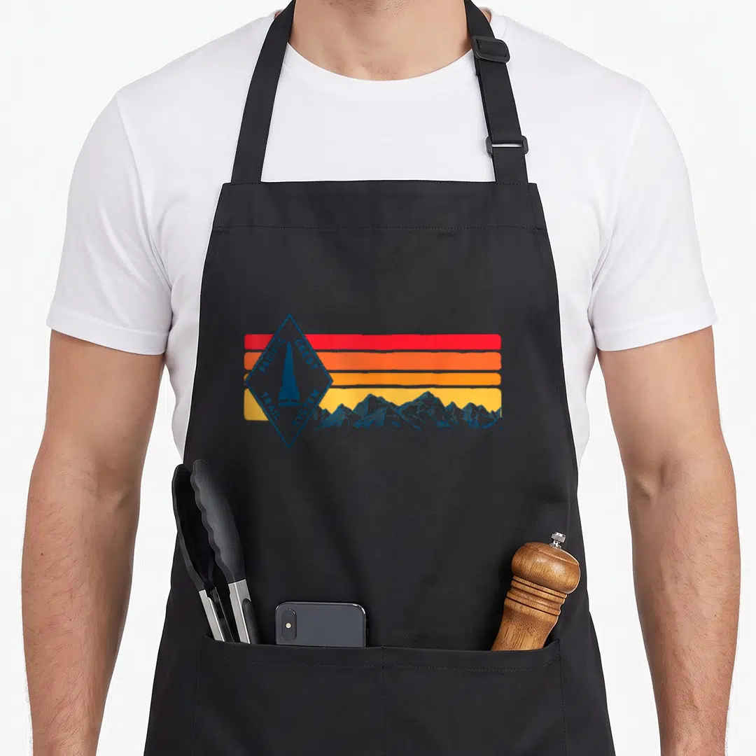 Pacific markers apron - Blue diamond sign reading Pacific Crest Trail System over red orange and yellow stripes — shown on a black cotton canvas apron against a white background