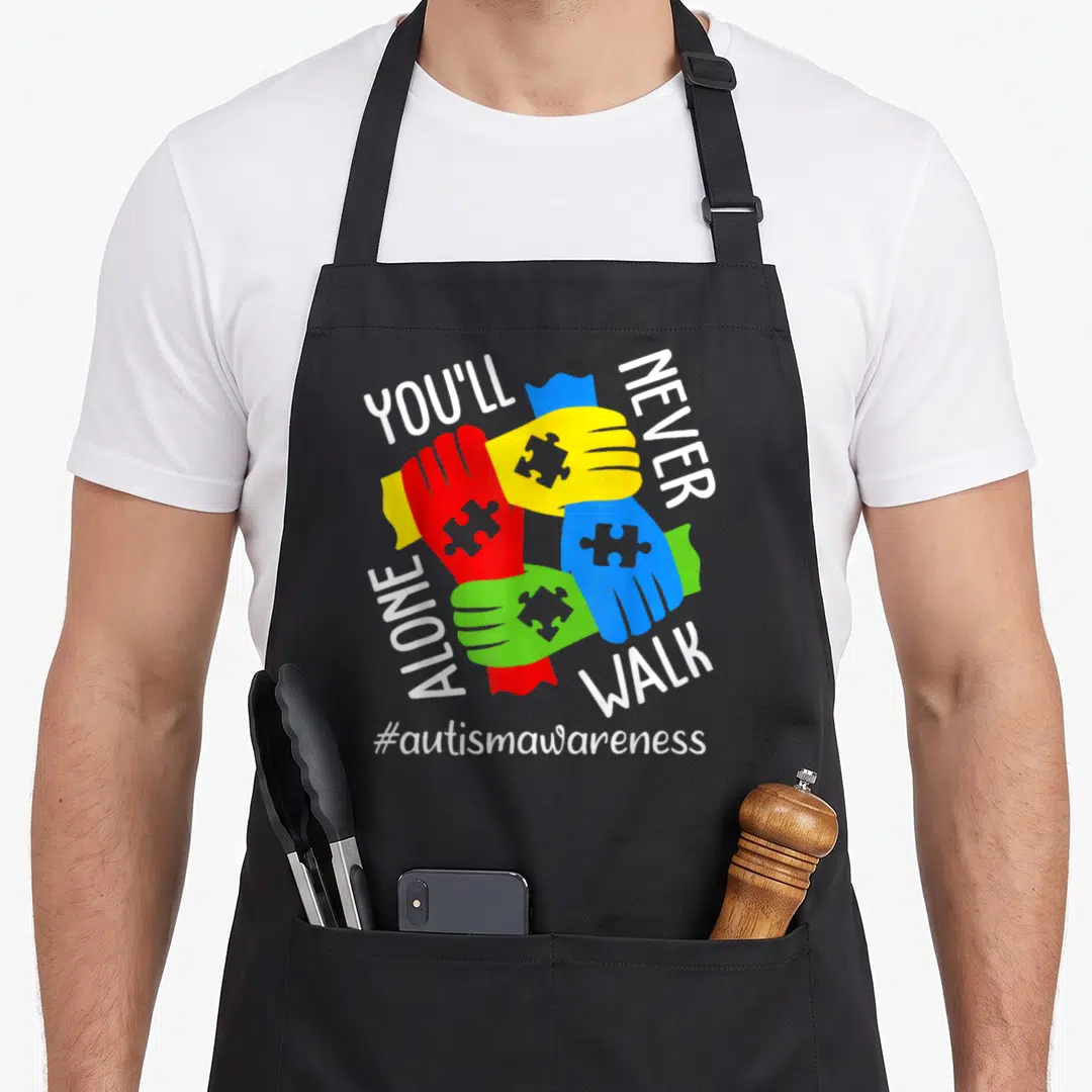 Autism youll never apron - Four interlocked hands in red yellow blue and green with puzzle piece details and awareness — shown on a black cotton canvas apron against a white background