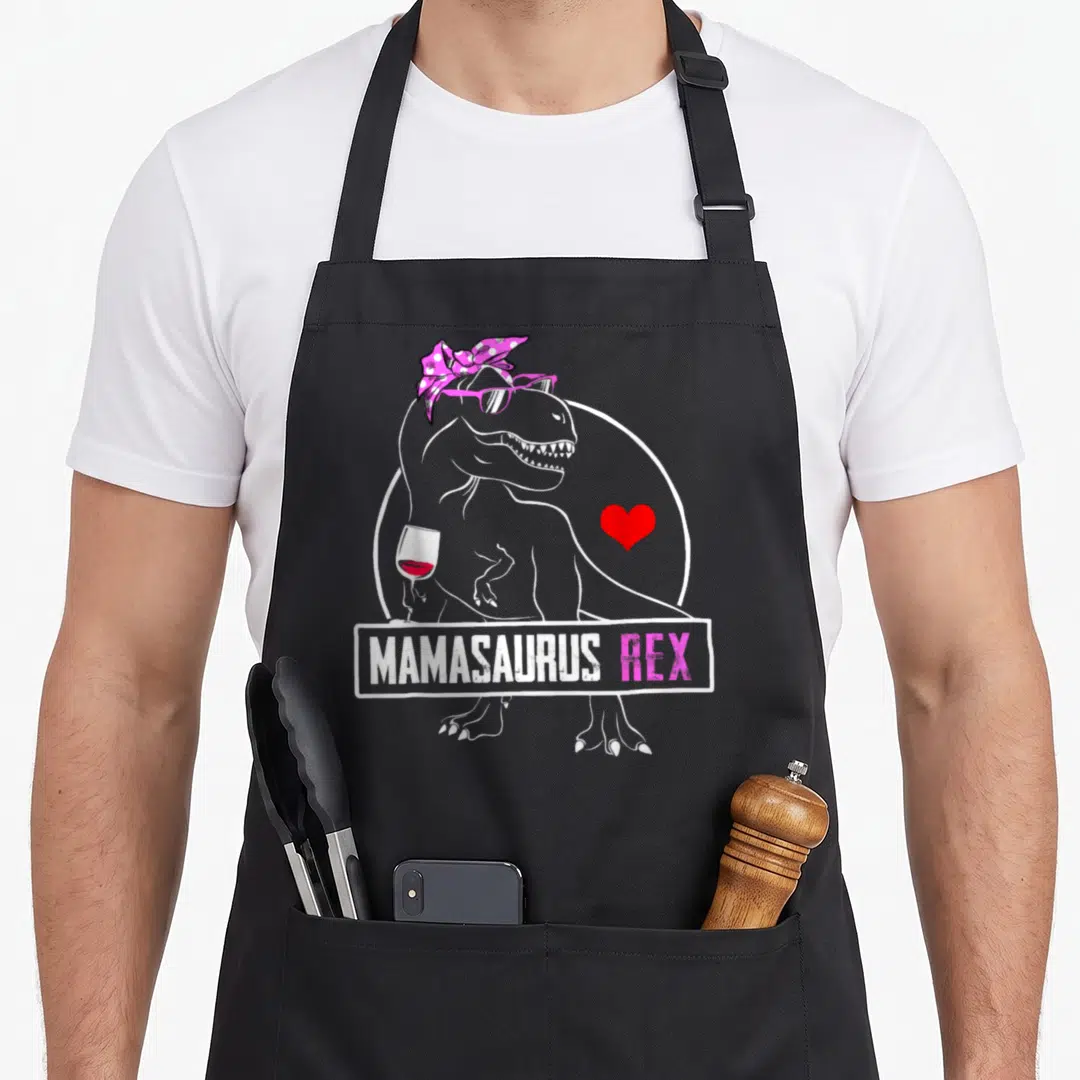 Mamasaurus dinosaur mama apron - Grey T-Rex wearing pink headband and sunglasses holding red wine next to red heart — shown on a black cotton canvas apron against a white background