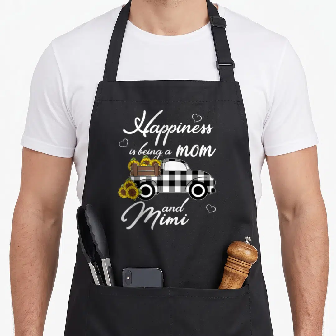 Mimi sunflower grandma apron - Pickup truck with sunflowers and text Happiness is being a mom and Mimi — shown on a black cotton canvas apron against a white background