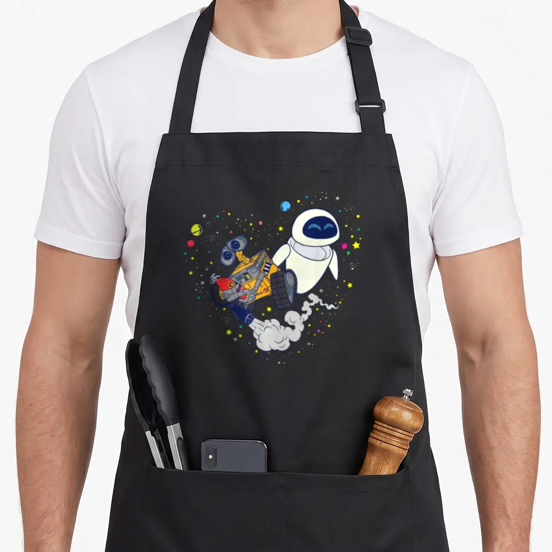 Planetary e.a apron - Eve and WALL-E floating in a heart of planets and stars with smoke trail — shown on a black cotton canvas apron against a white background
