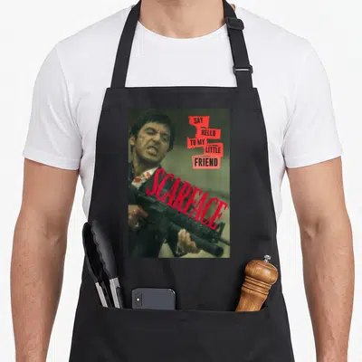 Scarface friends apron - Photo of man holding rifle with red text blocks saying Say Hello to My Little Friend Scarface — shown on a black cotton canvas apron against a white background