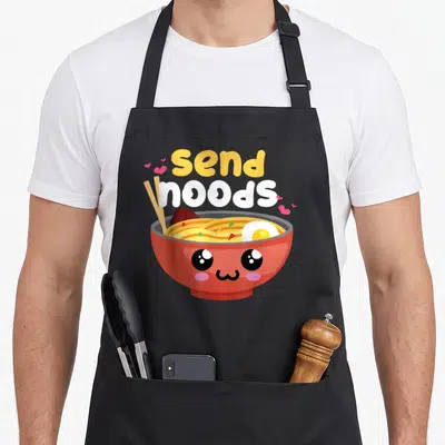 Ramen class funny apron - Cartoon red bowl with face, chopsticks, and send noods text surrounded by pink hearts — shown on a black cotton canvas apron against a white background