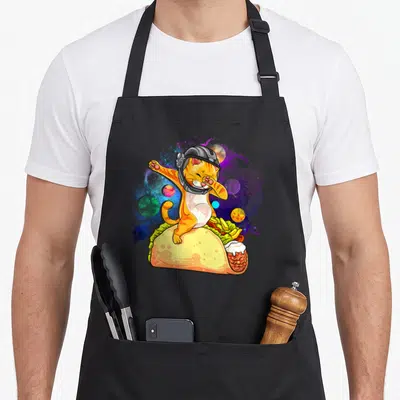 Dabbing space cat apron - Orange cat in helmet dabbing inside taco with space planets — shown on a black cotton canvas apron against a white background