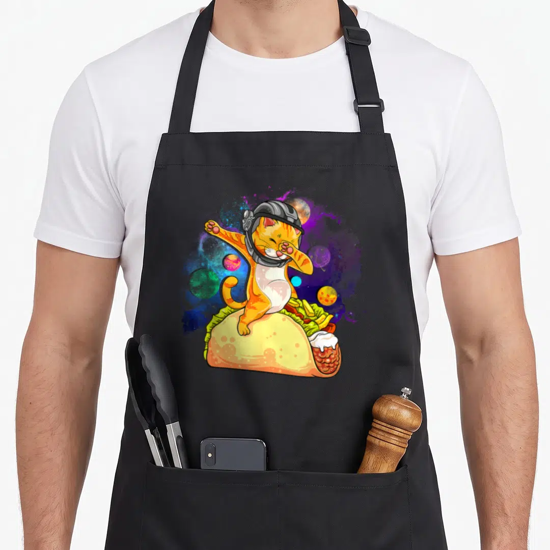Dabbing space cat apron - Orange cat in helmet dabbing inside taco with space planets — shown on a black cotton canvas apron against a white background