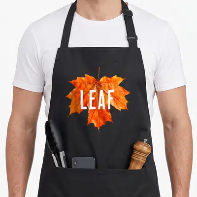 Leaf couple apron - Orange maple leaf with white LEAF text printed on fabric — shown on a black cotton canvas apron against a white background