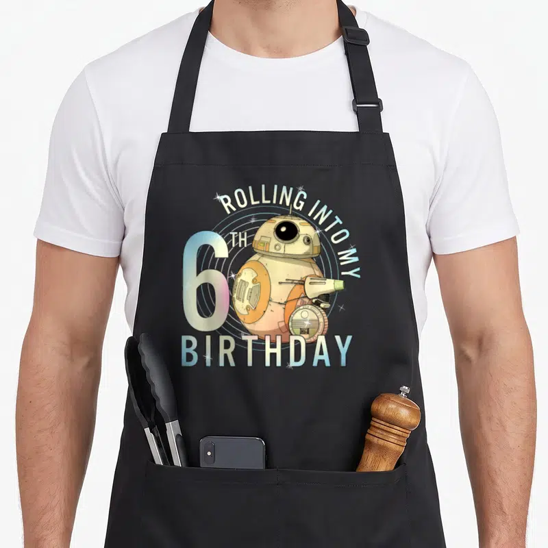Rolling 6th birthday apron - BB-8 droid with arched text and concentric circles — shown on a black cotton canvas apron against a white background