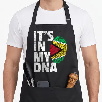 Guyana country apron - IT'S IN MY DNA text beside a fingerprint filled with Guyana flag colors in a distressed style — shown on a black cotton canvas apron against a white background