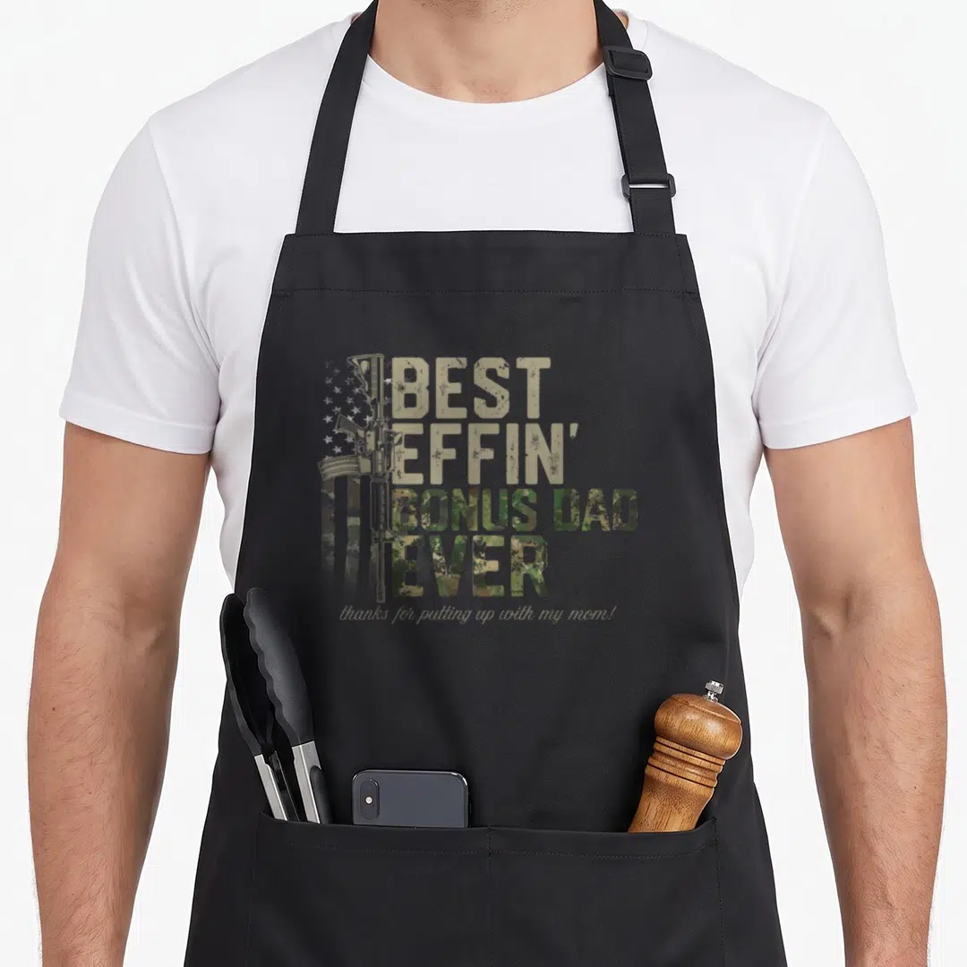 Effin camo apron - Rifle and camo flag with Best Bonus Dad Ever text and sarcasm script — shown on a black cotton canvas apron against a white background
