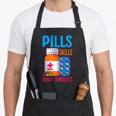 Pill pharmacist apron - Cartoon orange pill bottle with blue text and multi-colored pills on a black background — shown on a black cotton canvas apron against a white background