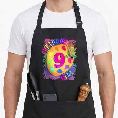 Painting birthday apron - Yellow artist palette with pink 9 and multicolored BIRTHDAY GIRL text surrounded by paint — shown on a black cotton canvas apron against a white background