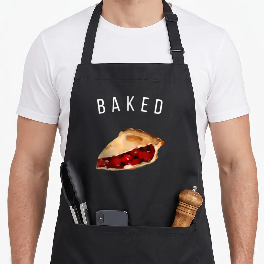 Baked cherry apron - White BAKED text above a realistic golden brown and red cherry pie slice — shown on a black cotton canvas apron against a white background