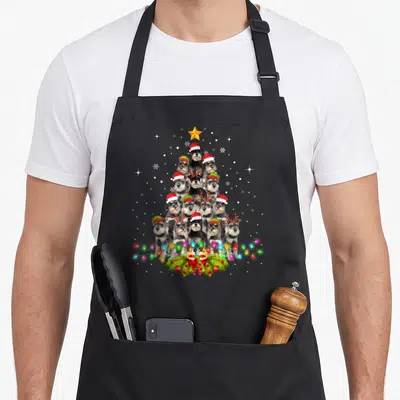 Schnauzer christmas tree apron - Twelve grey dogs in triangle formation with yellow star, holly, and colored lights — shown on a black cotton canvas apron against a white background