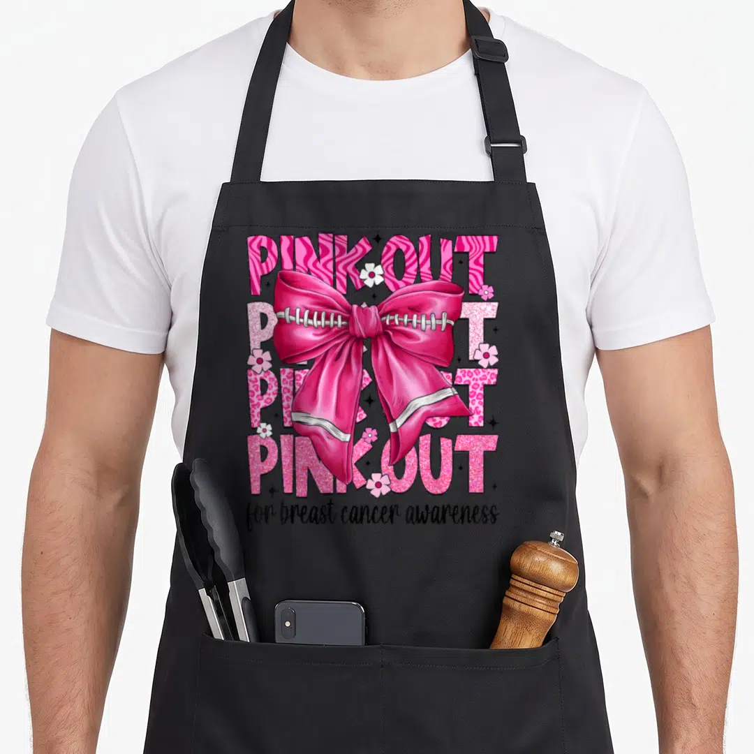 Coquette bow breast cancer awareness aprons - Large pink bow with football laces over four lines of PINK OUT text — shown on a black cotton canvas apron against a white background
