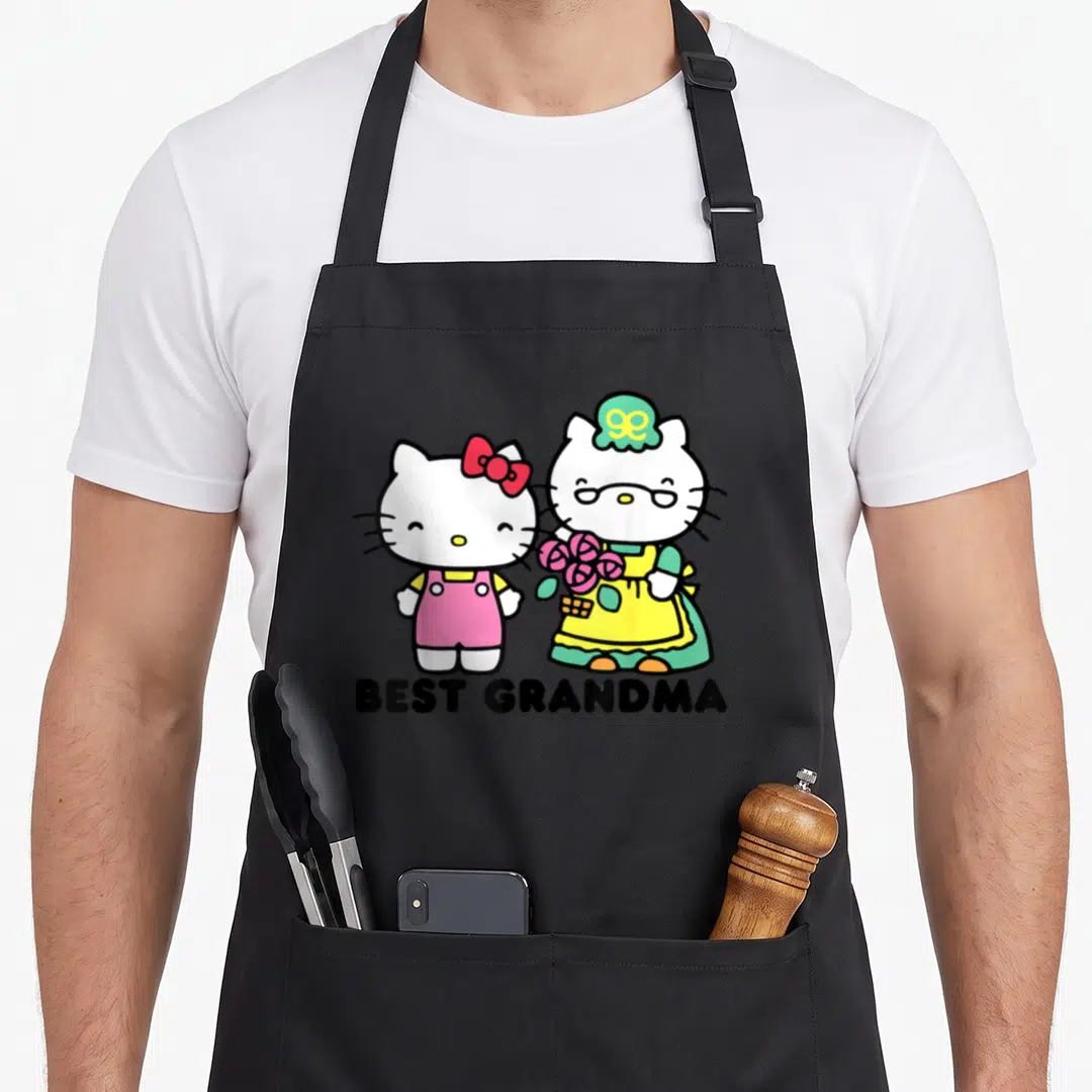 Vintage grandma apron - Two white cartoon cats standing side-by-side above black BEST GRANDMA text in pink and yellow — shown on a black cotton canvas apron against a white background