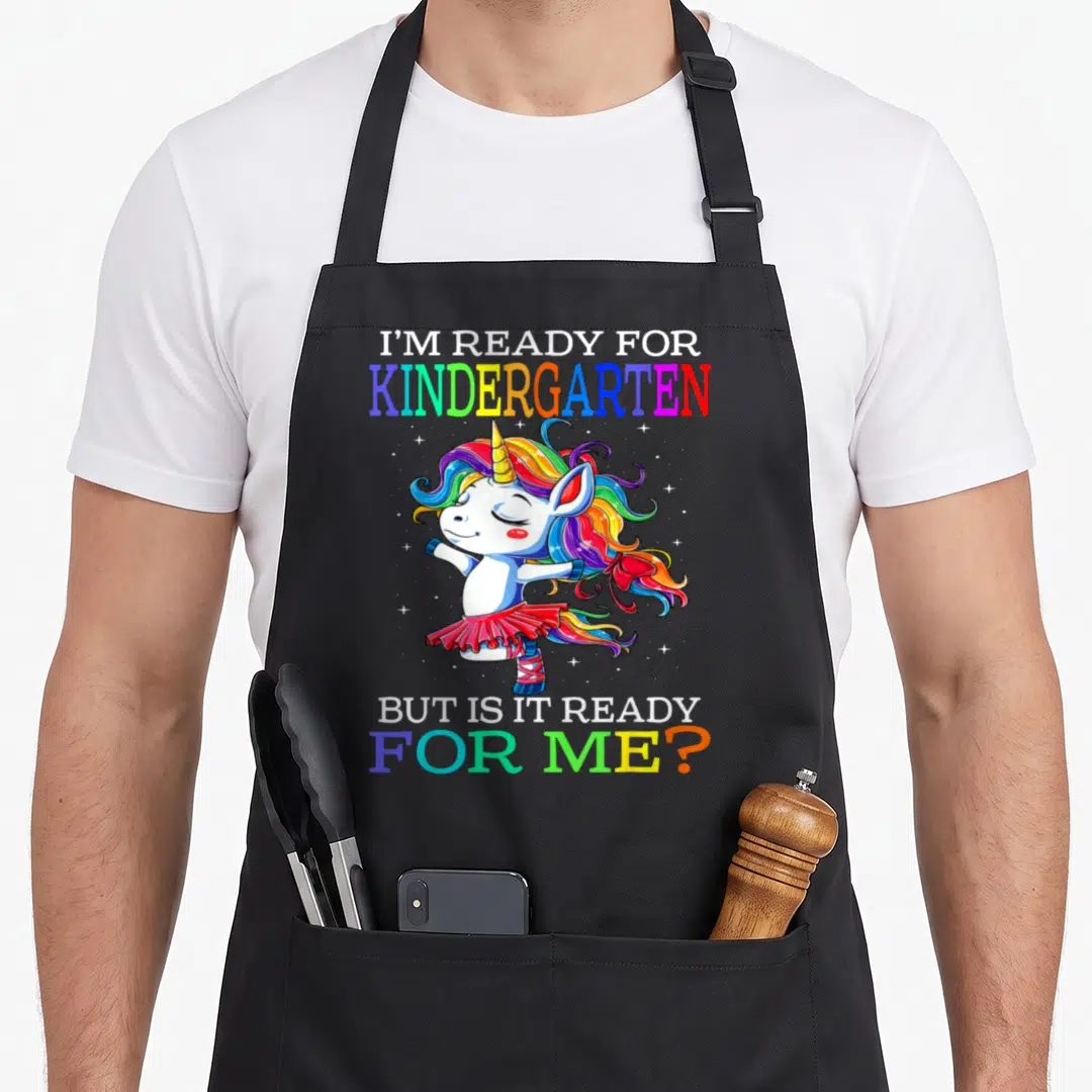Ready kindergarten unicorn aprons - Cartoon unicorn in red tutu with rainbow mane and split text quote — shown on a black cotton canvas apron against a white background