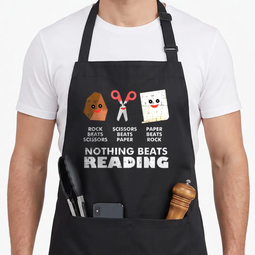 Beat reading books apron - Rock paper scissors characters with text Nothing Beats Reading on grey background — shown on a black cotton canvas apron against a white background
