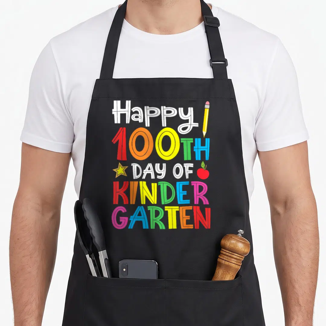 100th kindergarten teacher apron - Stacked colorful text Happy 100TH Day of Kinder Garten with pencil star and apple — shown on a black cotton canvas apron against a white background